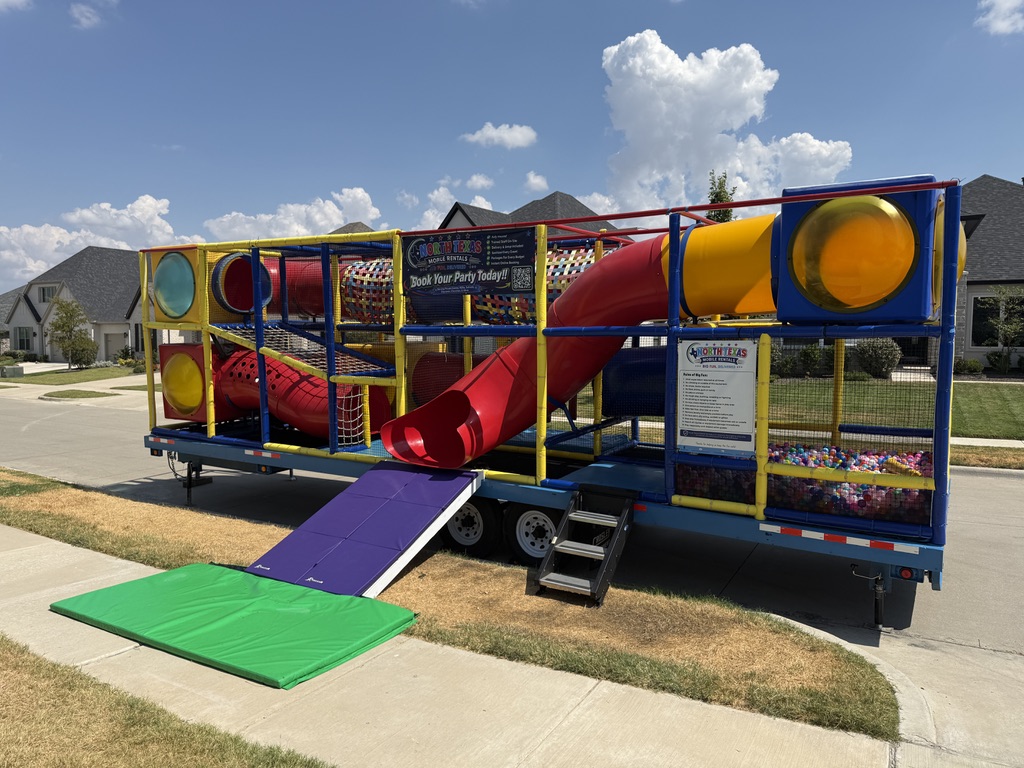 Signature Mobile Playground trailer with a red tube slide, tunnels, and ball pit set up at the curb in a North Texas neighborhood